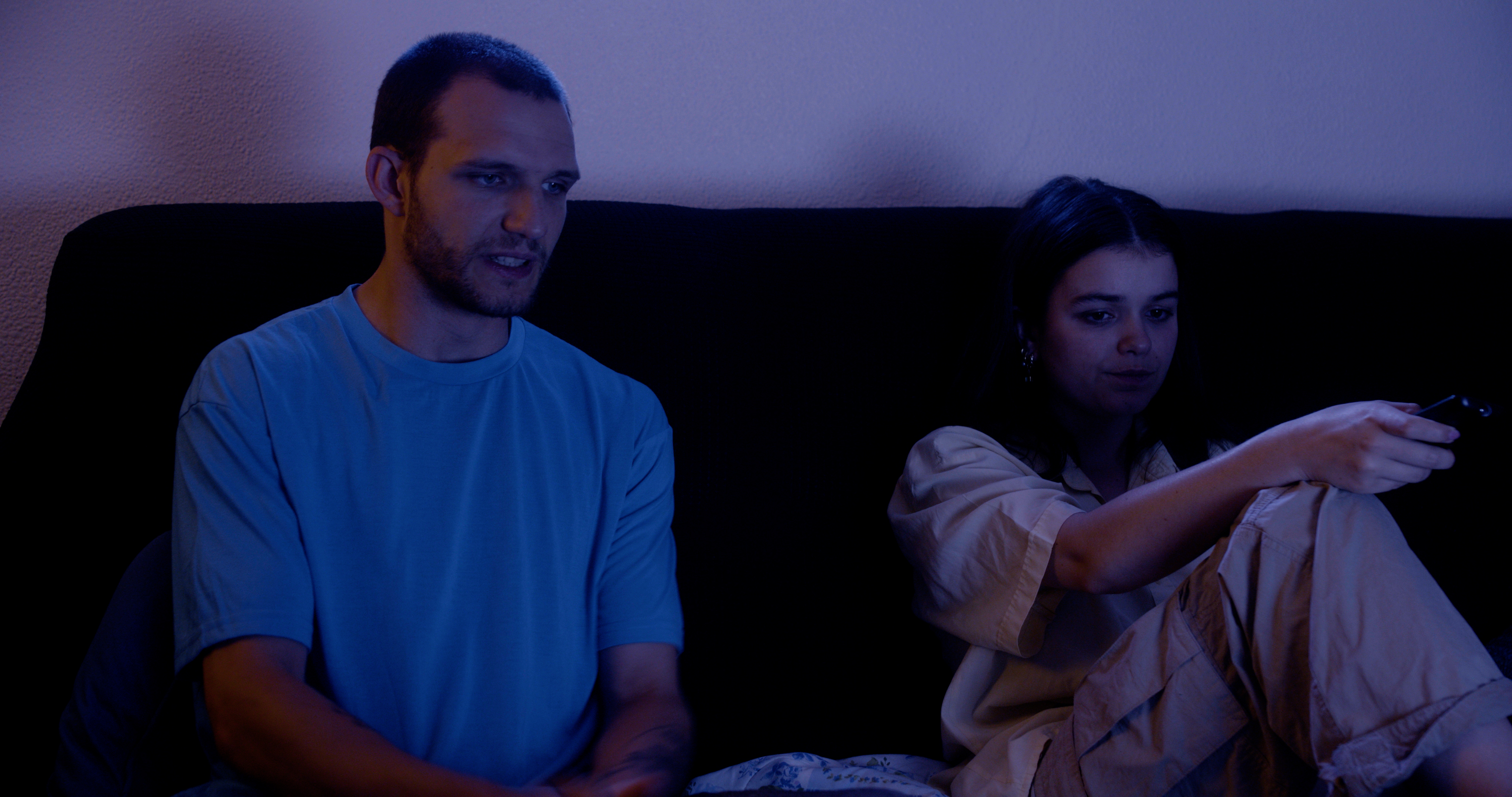 Male and female couple changing the channels on the television while sat on the sofa.